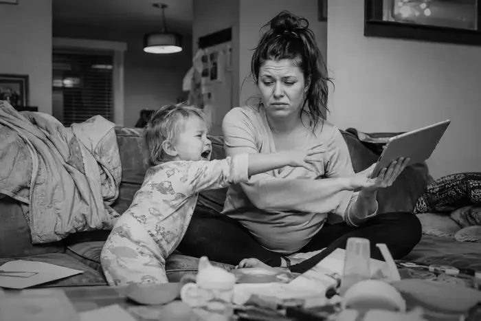 Stressed parent with toddler having a meltdown next to a tablet
